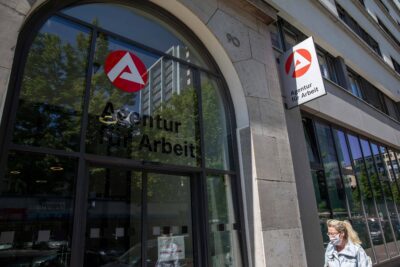 A masked woman walking in front of an employment agency in Berlin.