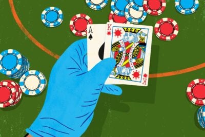 A hand wearing a blue surgical glove holding poker cards, depicting the suicide king in the suit of a COVID virus particle.